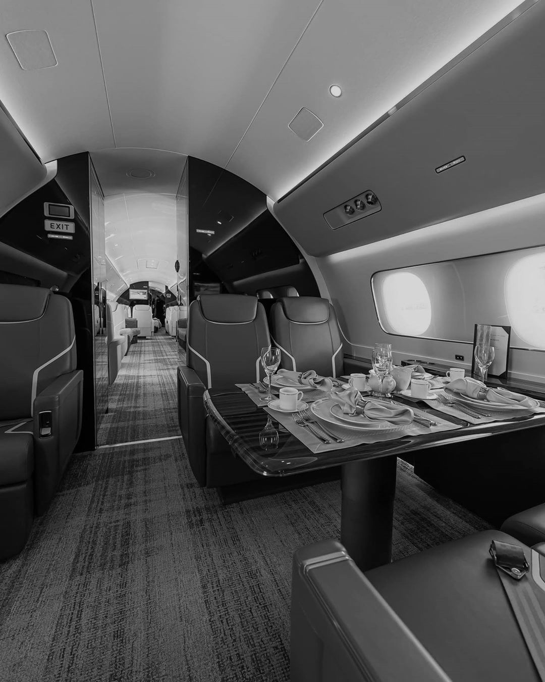 A private jet cabin with a dining table laid for four and leather seats along the aisle