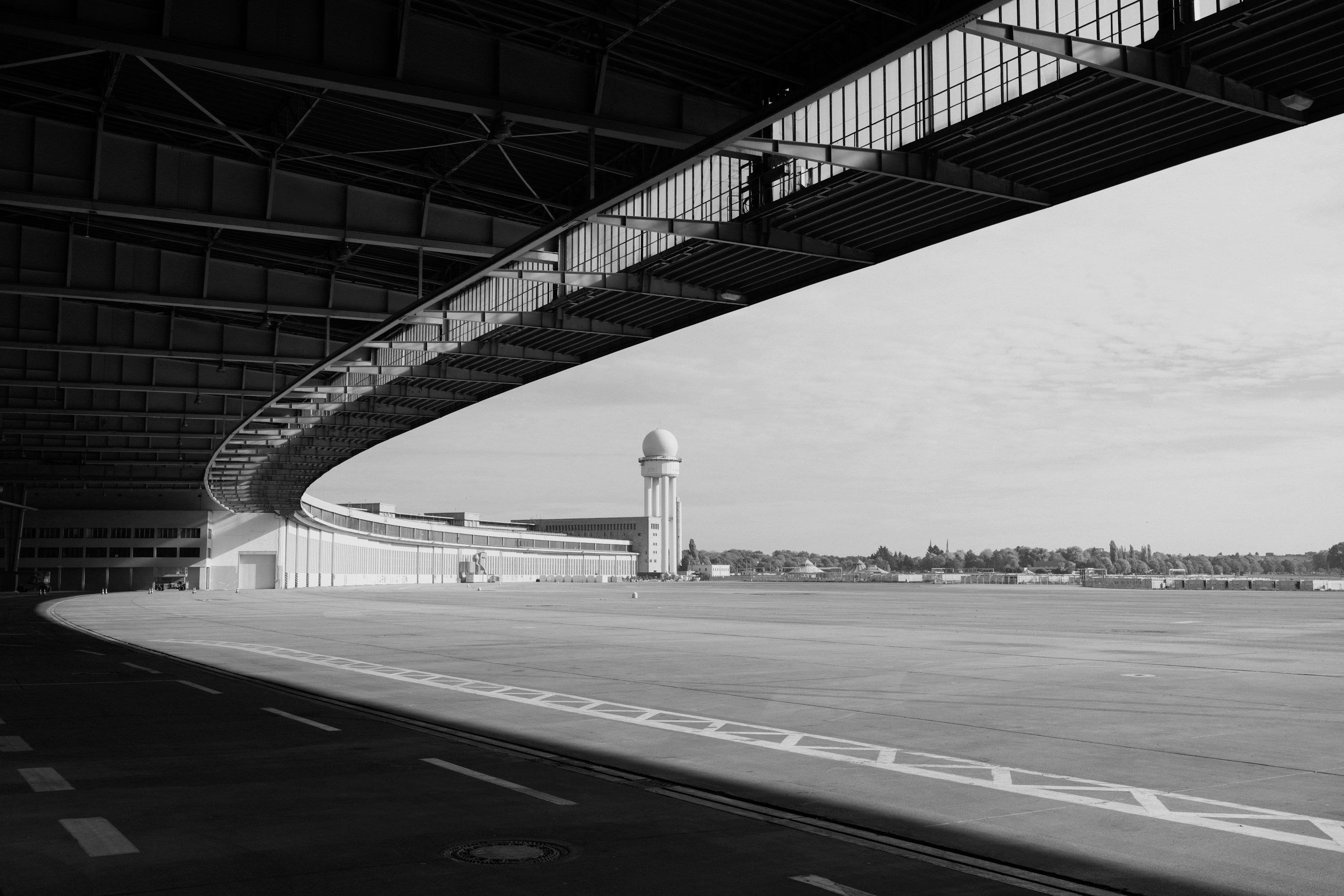 An airport apron seen from under a curved hangar roof, with the control tower beyond