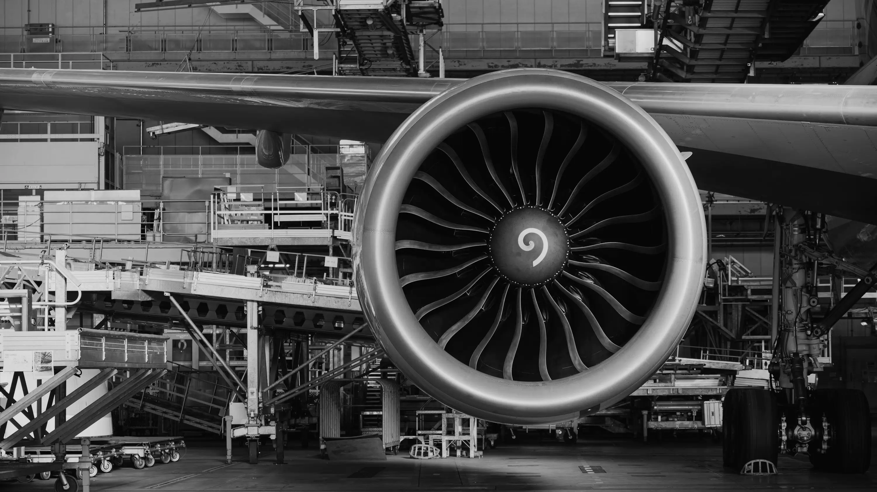 A jet engine on the wing in a maintenance hangar, with work platforms behind